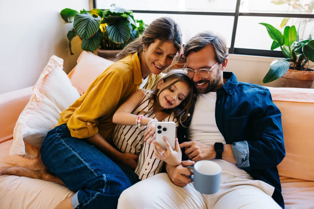 Parents and their daughter smiling together while looking at a phone on the sofa