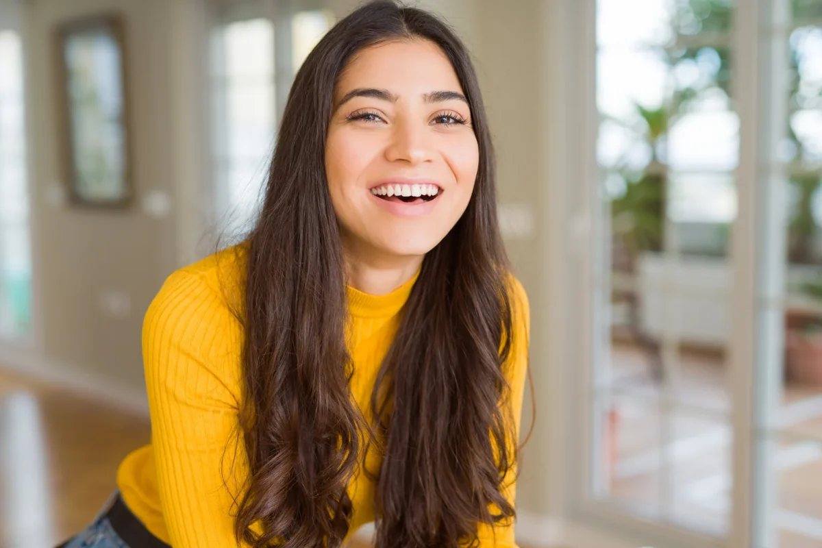 Smiling woman with long dark hair wearing a yellow sweater
