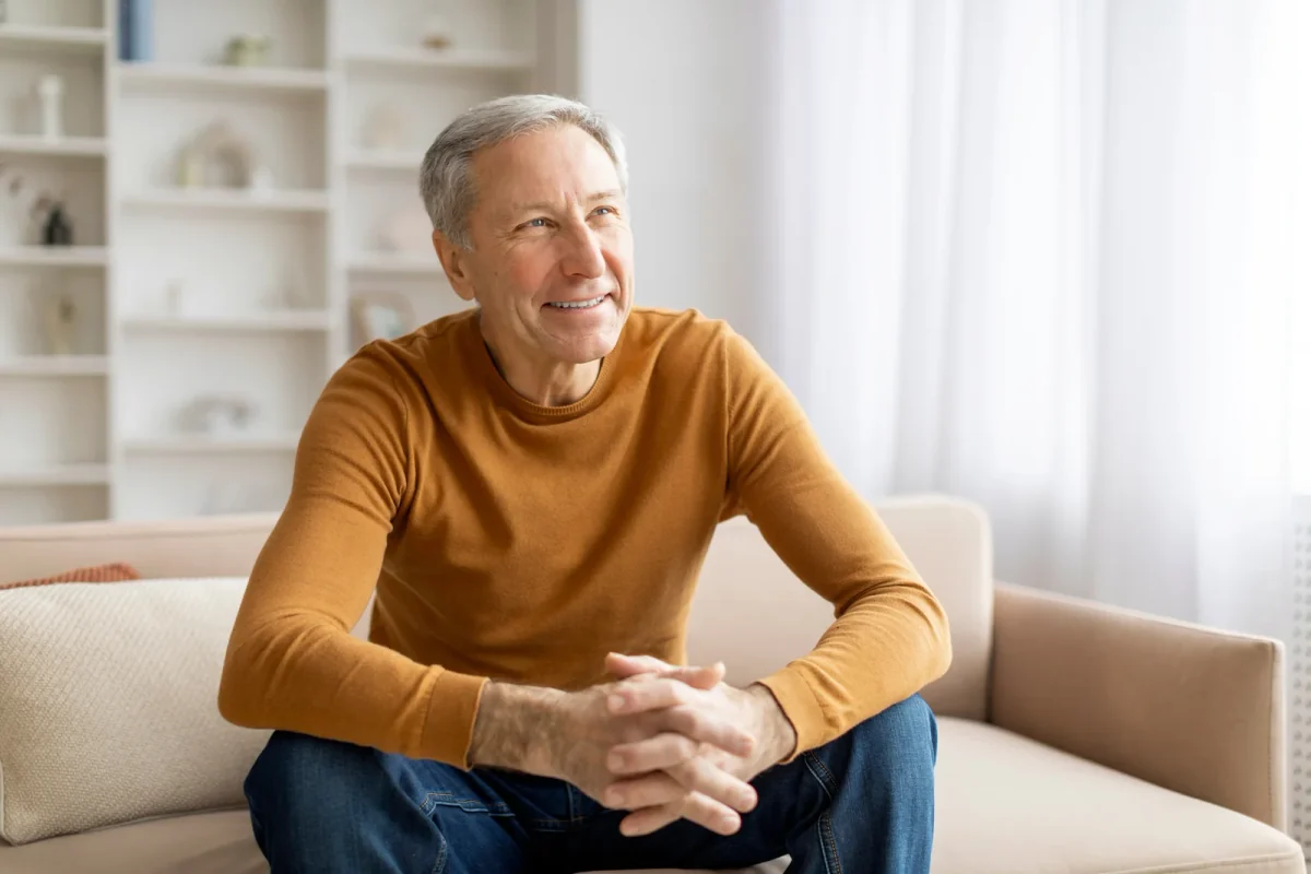 Smiling man in a mustard sweater seated on a sofa